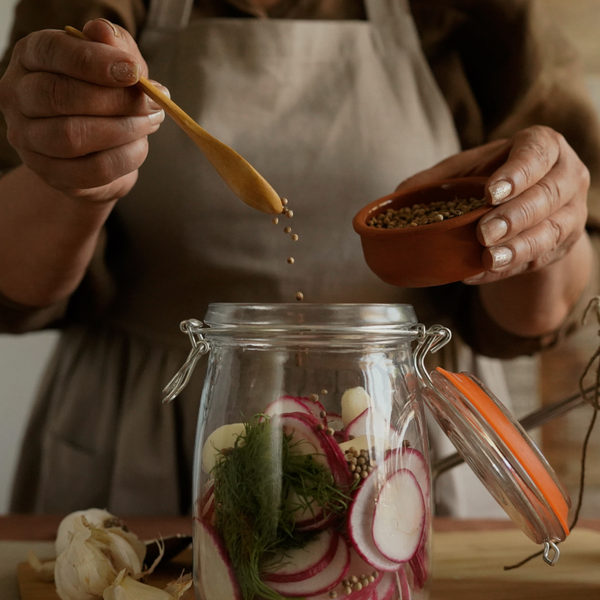 Someone in a rustic kitchen filling a pickling jar with ingredients